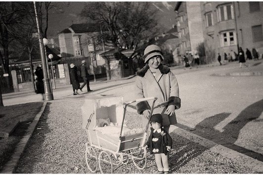 Ein junges Mädchen mit Spielzeugpuppe und Kinderwagen