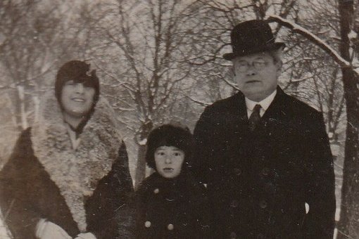 Familie im Winter, ein Kind steht auf einem Rodel