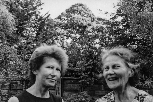 Eine ältere Frau und ihre Tochter stehen gemeinsam in einem Garten