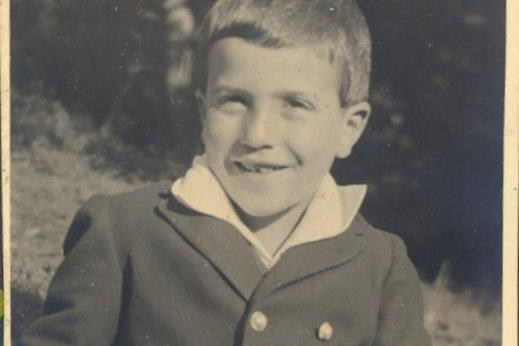 Ein junges Kind sitzt auf einer Wiese in Trachtenanzug