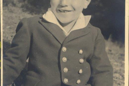 Ein junges Kind sitzt auf einer Wiese in Trachtenanzug