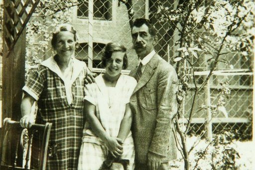 Eine ältere Frau, ein Herr und eine jonger Frau mit einem Hund zwischen den Beinen stehen gemeinsam im Garten