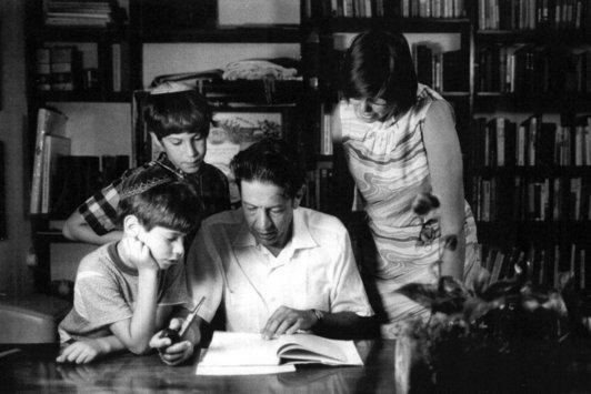 Ein Mann sitzt an einem Schreibtisch, seine Ehefrau und seine zwei Kinder stehen neben ihm