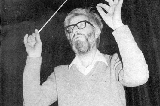 Ein älterer Herr mit dichtem Bart steht mit Taktstock and einem Dirigentenpult