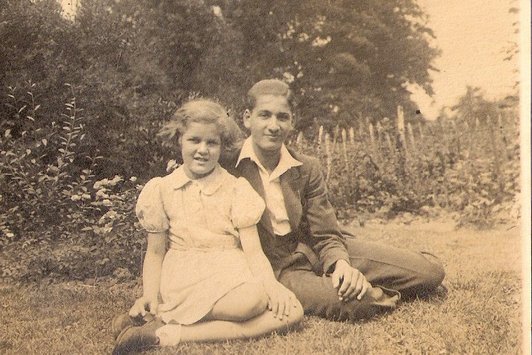 Ein junges Mädchen und ihr älterer Bruder sitzen auf einer Wiese