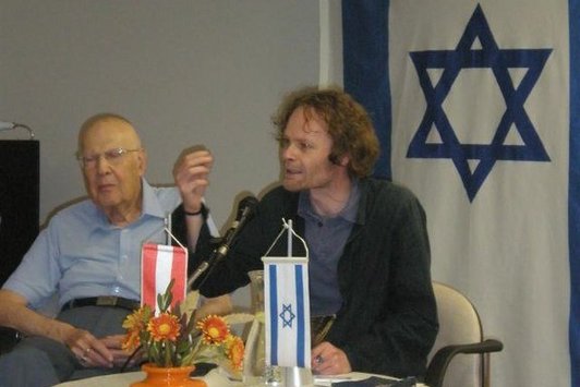 Zwei Herren sitzen an einem Tisch, auf dem Tisch ist eine Österreichflagge und eine Israelflagge zu sehen