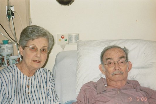 Eine ältere Frau sitzt neben einem im Krankenbett liegenden Herren