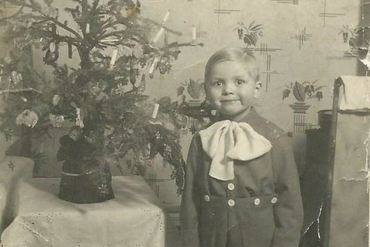 Ein junger Bub steht neben einem Weihnachtsbaum