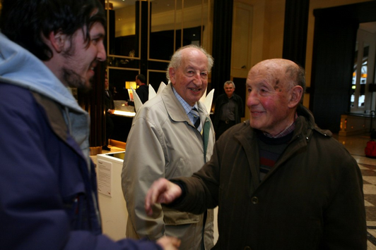 Ein älterer Herr und ein jüngerer Mann unterhalten sich, ein weiterer älterer Mann steht hinter ihnen