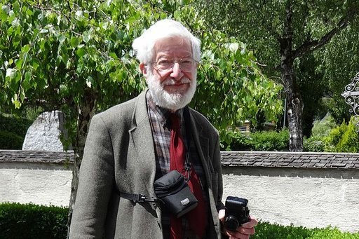 Ein älterer Herr hält eine Kamera und steht in einem Park