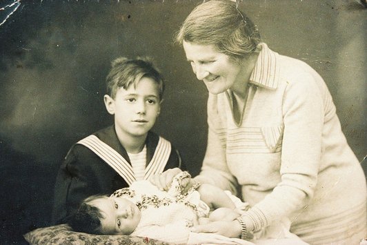 Eine ältere Dame steht neben einem jungen Buben, während sie ein Baby hält